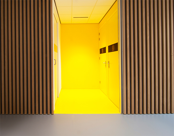 Interieur ontwerp van moderne tijdloze huisartsen praktijk te Joure. Signaal gele toiletgroep met betonlookvloer en eikenhouten wandafwerking.