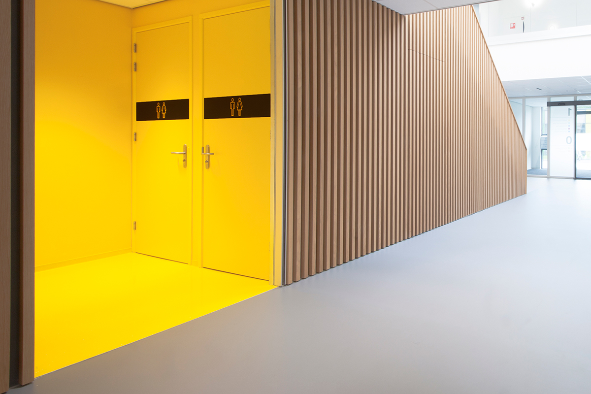 Interieur ontwerp zorgcomplex de Werf te Joure door Studio Doccia. Royale entree met maatwerk eikenhouten wandbekleding, betonlook vloer en signaal gele toiletruimte.